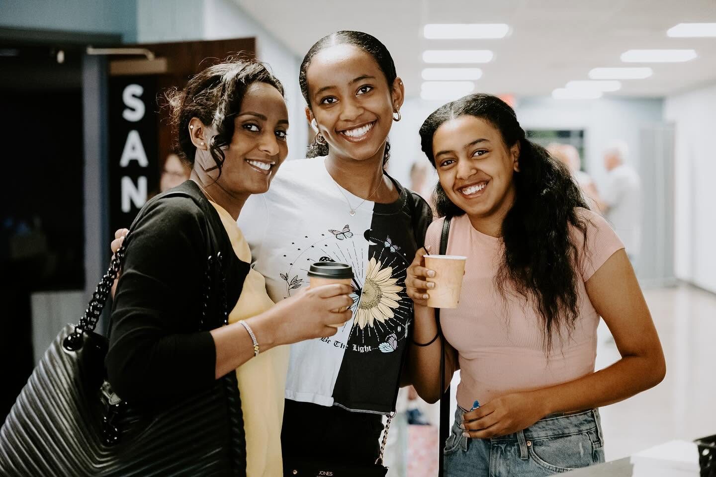 Three young women from Emmanuel gathered together, smiling with coffee in hand